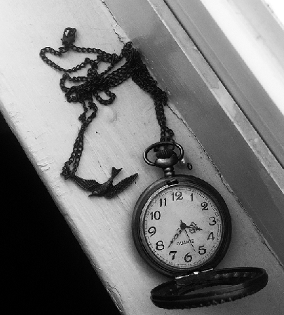 A black and white photo of an open pocket watch. The chain has a bird charm attached to it.